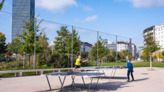 Deux personnes jouent au ping-pong en extérieur.