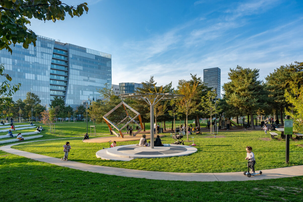 Parc urbain avec enfants jouant, bâtiments modernes.