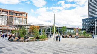 Place animée avec buildings et passants en journée.