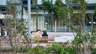 Personnes assises sur un banc devant un bâtiment.